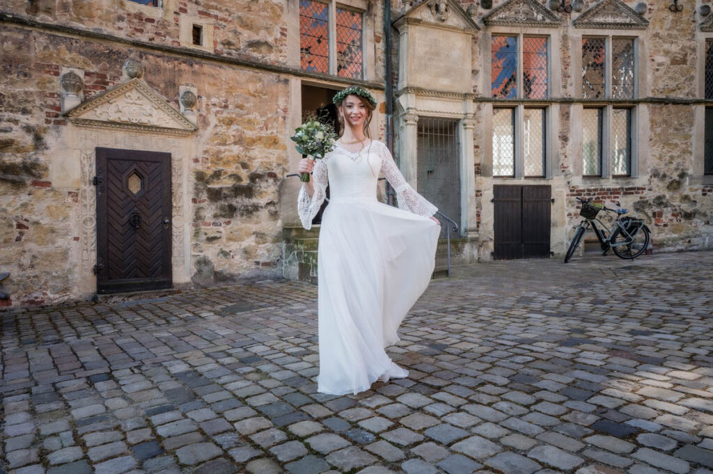 Braut im Hochzeitskleid steht vor einem alten Haus