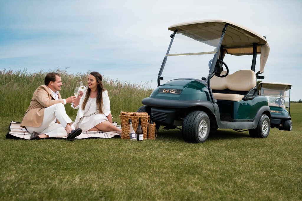 verliebtes Paar picknickt auf einem Golfplatz und trinkt Sekt