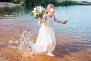 Mädchen im Hochzeitskleid läuft durch das Wasser mit einem Blumenstrauß in der Hand