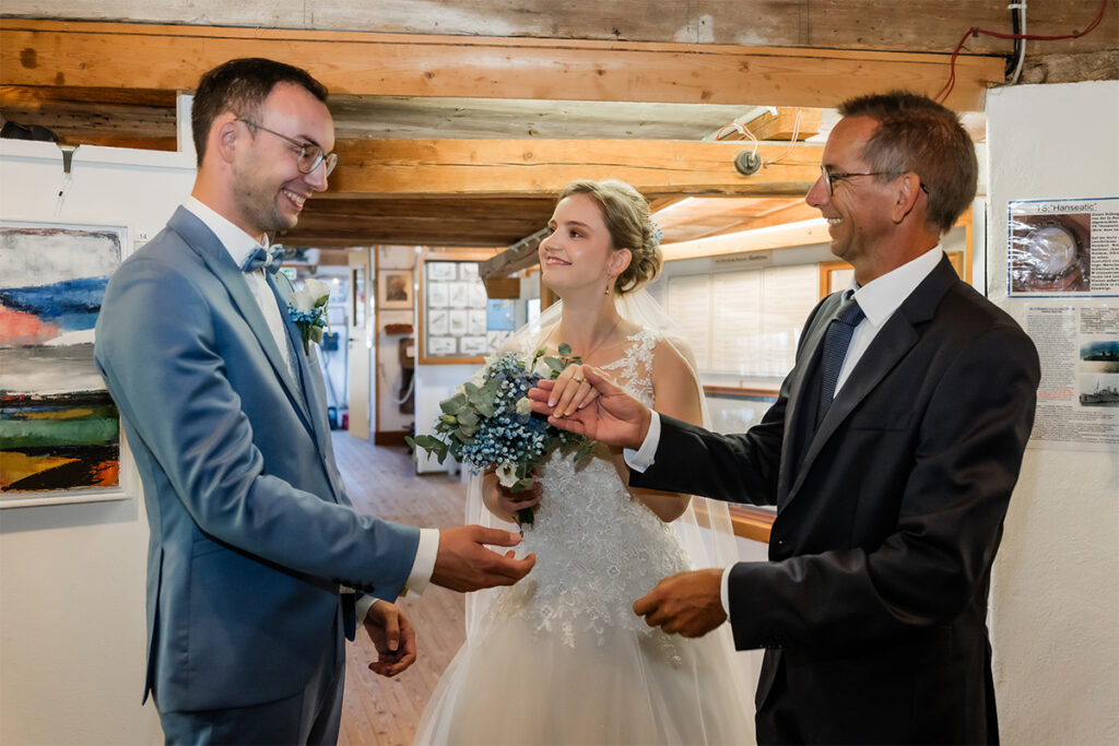 Brautvater übergibt seine Tochter an den lachenden Bräutigam
