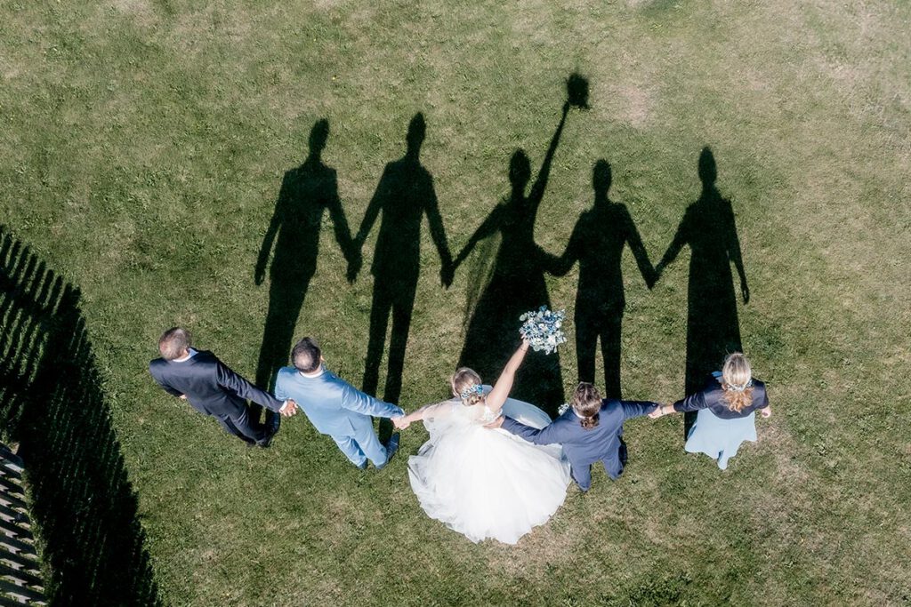 Luftbildaufnahme von einer Hochzeitsgesellschaft auf einer Wiese mit Brautstrauß