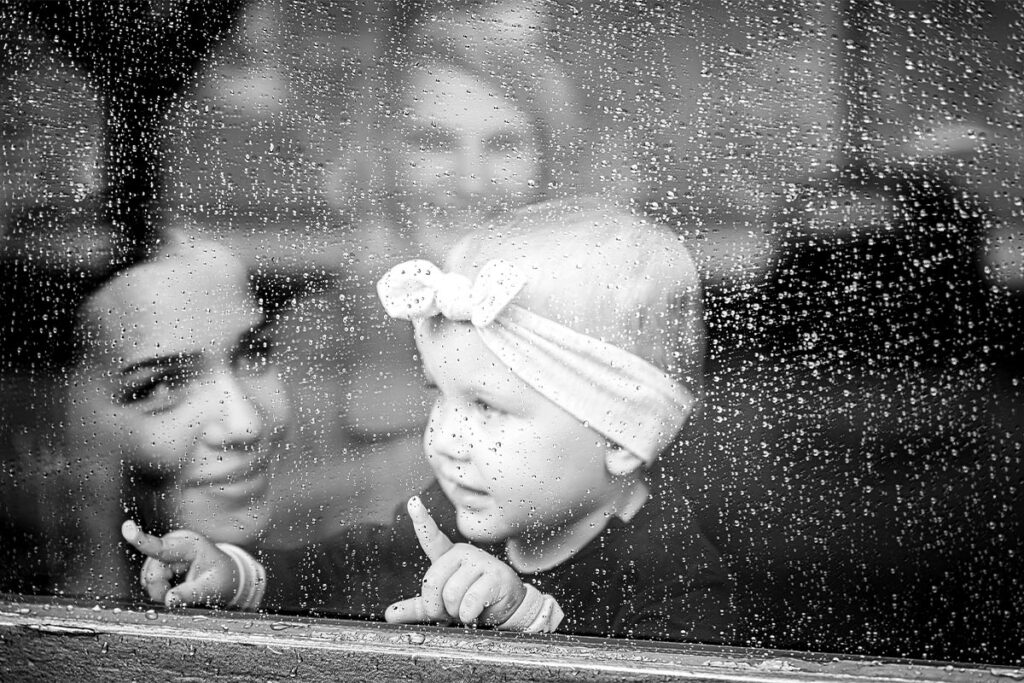 ein Kleinkind schaut wärend einer Hochzeitsfeier aus dem Fenster. Regenhochzeit