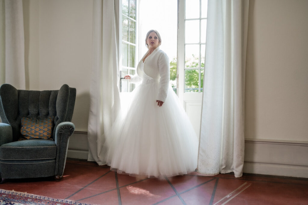 Braut steht an der Balkontür im Hochzeitskleid