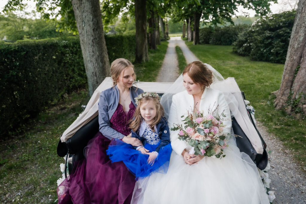 Hochzeitskutsche mit Braut und Schwester vor einem Schloss