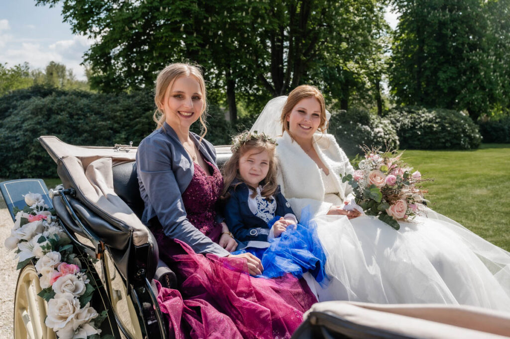 Braut, Schwester und Tochter in der Hochzeitskutsche fahren durch die Natur