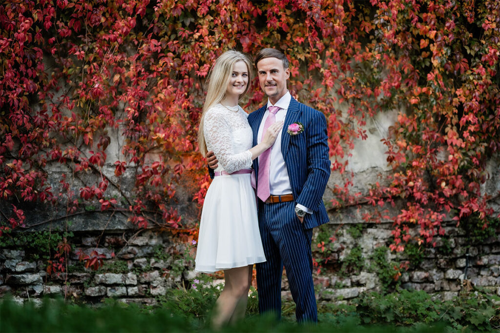 Brautpaar steht Arm in Arm vor einem roten Busch