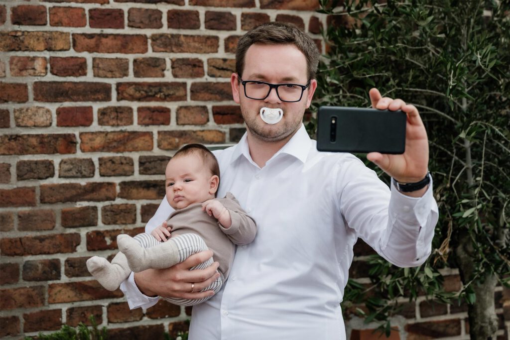 Hochzeitsfotograf Essen fotografiert einen Vater mit Schnuller im Mund und Baby im Arm