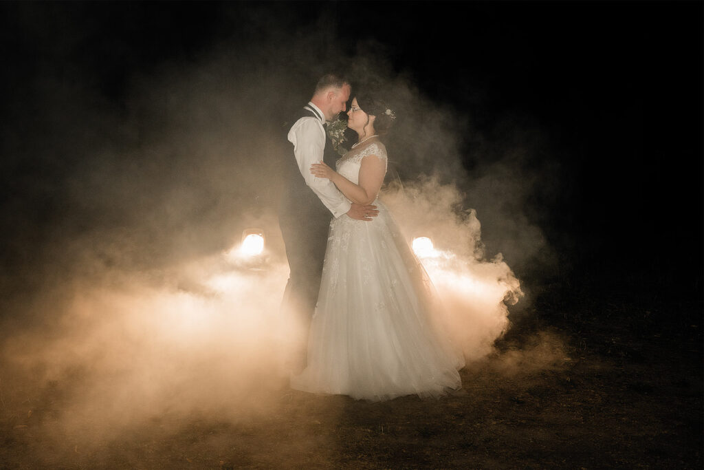 Brautpaar steht im Rauch und wird von den Lichtern des Hochzeitsauto angestrahlt