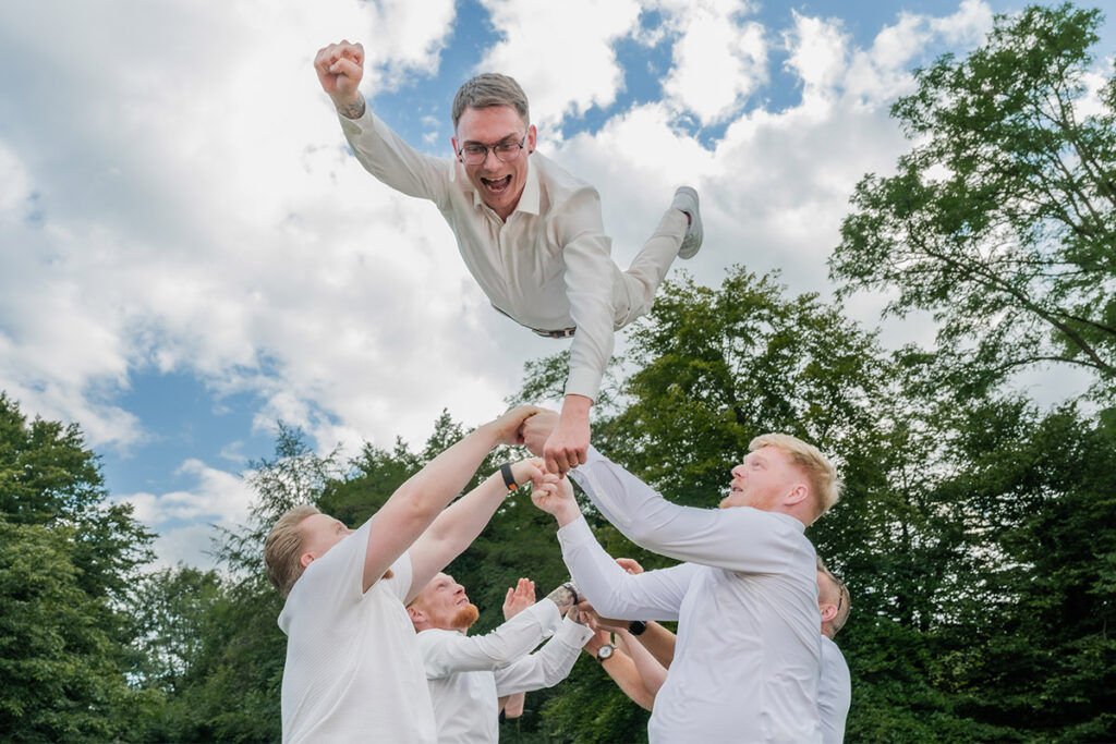 Bräutigam wird von Hochzeitsgästen hochgeworfen