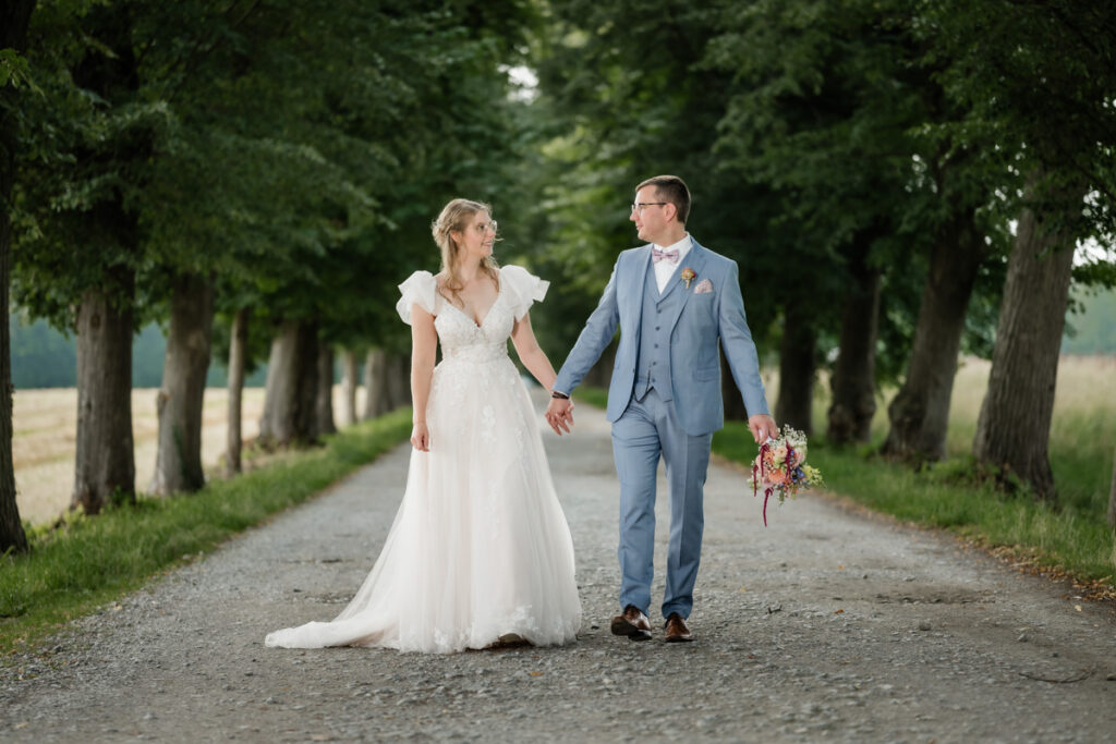 hochzeitsfotograf nrw fotografiert ein Brautpaar, dass durch eine Baumallee spaziert