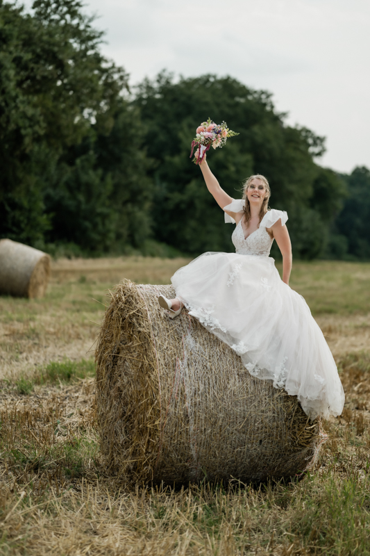 Braut sitzt auf einem Strohballen im Strohfeld