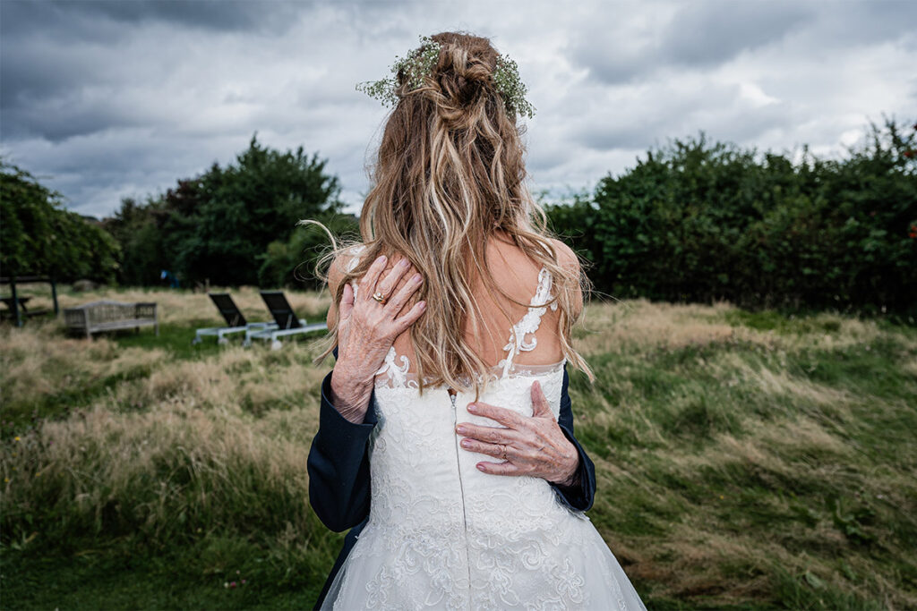 Braut im Spitzenkleid wird liebevoll von ihrer Großmutter umarmt