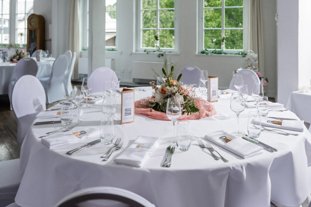 Elegante Tischdekoration für eine Hochzeit im Romantik Hotel Neuhaus Iserlohn, festlich gedeckte runde Tische mit Blumengestecken in Rosa und Weiß
