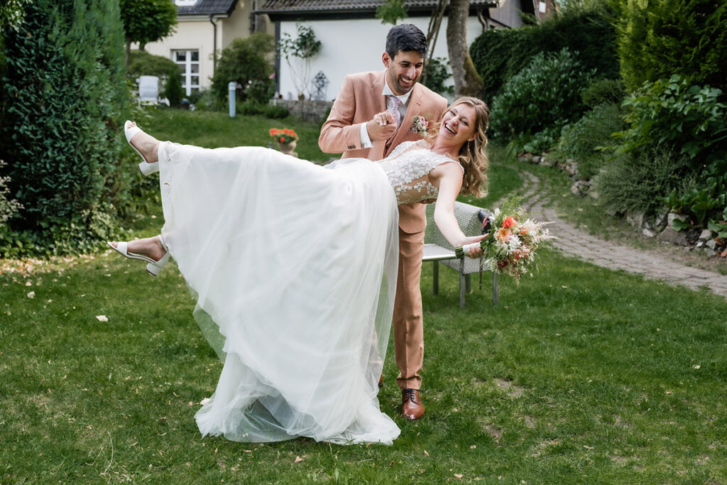 Brautpaarshooting im Garten des Romantik Hotel Neuhaus Iserlohn, Bräutigam hebt lachende Braut hoch, Hochzeitsfotografie Andreas Zabel