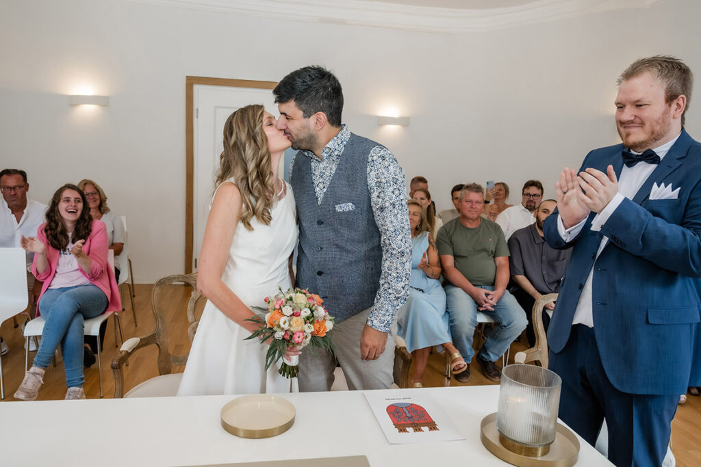 Brautpaar küsst sich nach dem Ja-Wort im Standesamt Herdecke während die Gäste applaudieren, Hochzeitsfotografie von Andreas Zabel