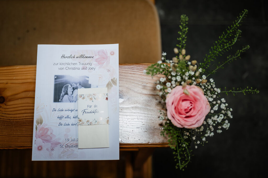 Detailaufnahme eines personalisierten Kirchenhefts mit der Aufschrift 'Für die Freudentränen' und einer rosa Rose in der St. Elisabeth Kirche Herdecke