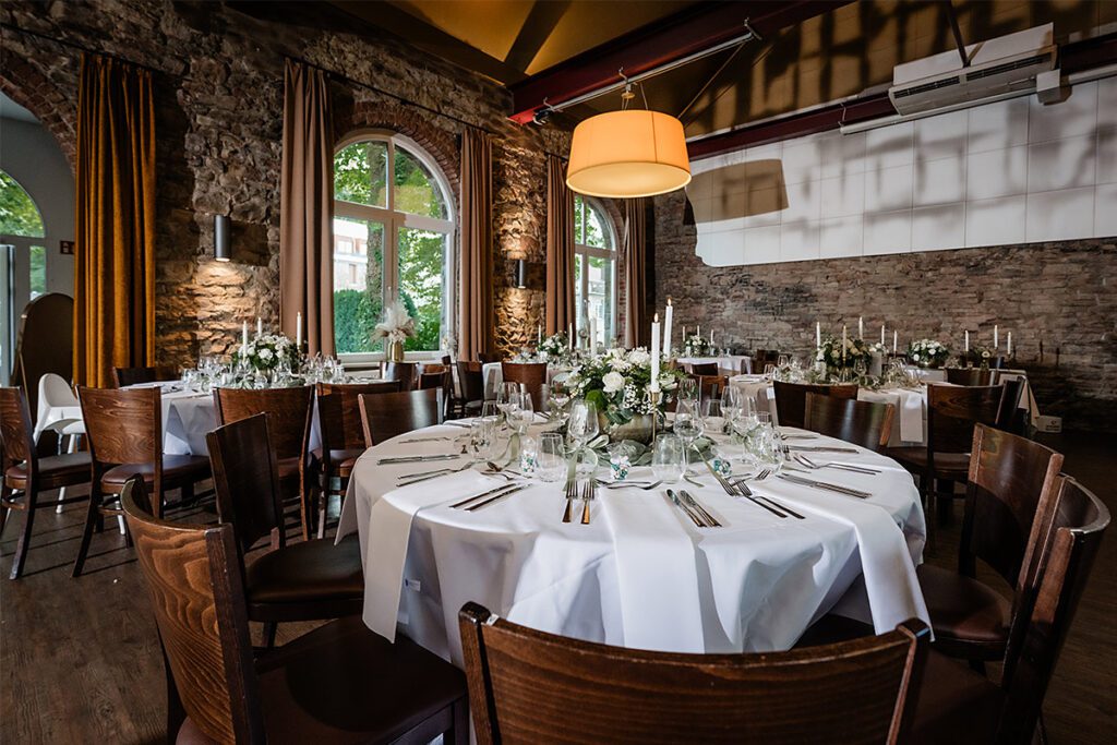 Stimmungsvoll beleuchteter Festsaal für eine Hochzeit in Essen mit eingedeckten Festtafeln und Backstein-Mauerwerk