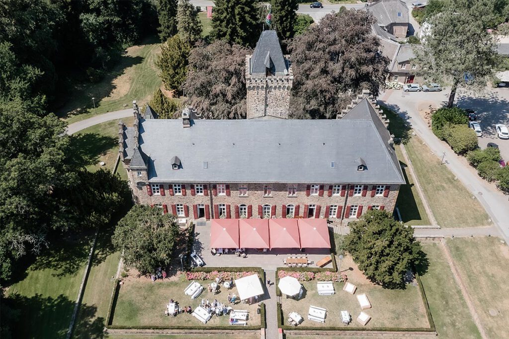 Drohnenaufnahme einer Schloss-Hochzeitslocation in Essen mit festlich gestaltetem Außenbereich und Parkanlage