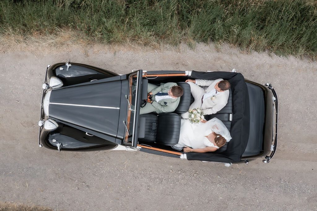 Kreative Drohnenaufnahme von oben: Hochzeitsauto-Oldtimer mit Brautpaar und Chauffeur bei einem Shooting in Essen